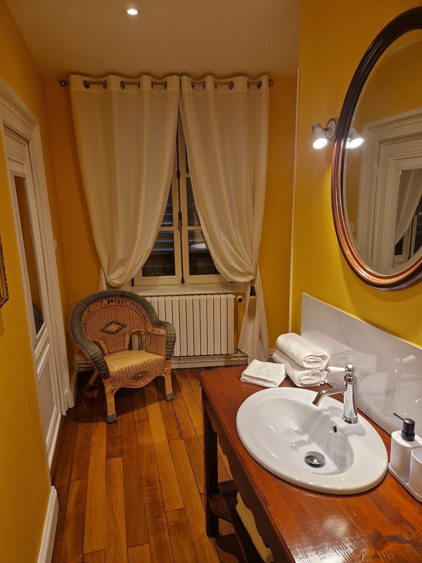 Salle d’eau privative de la chambre La Bagatelle, murs safran et miroir ovale